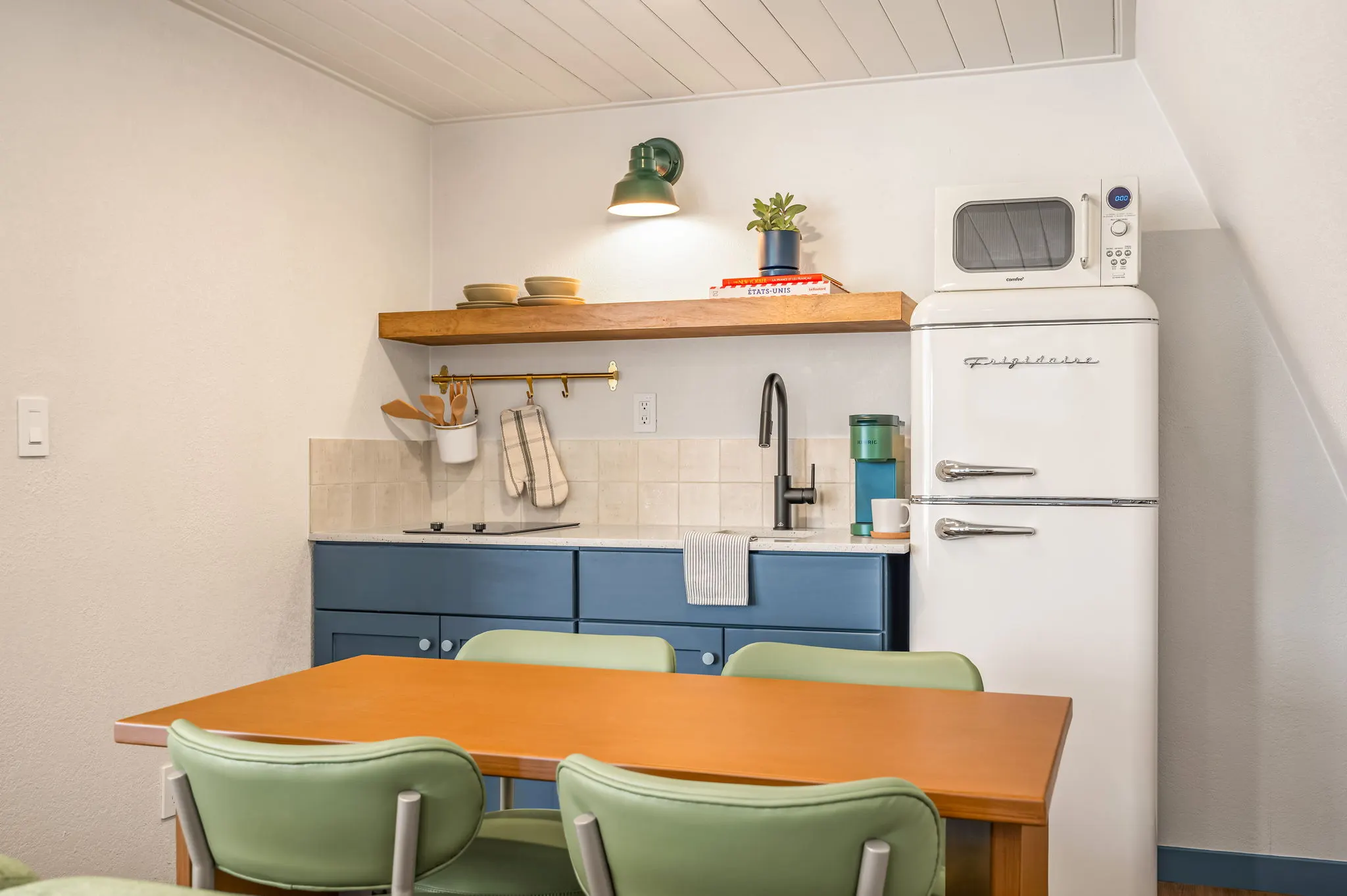 Kitchenette with blue cabinets, retro fridge and green chairs, Petit Cowboy