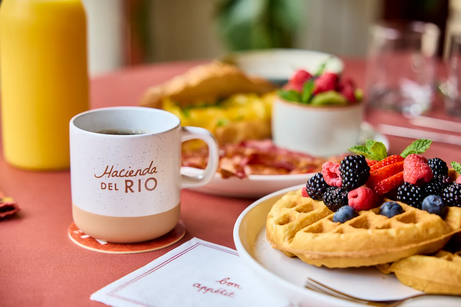 A Hacienda del Rio mug beside waffles with berries and a carafe of orange juice, Del Sol