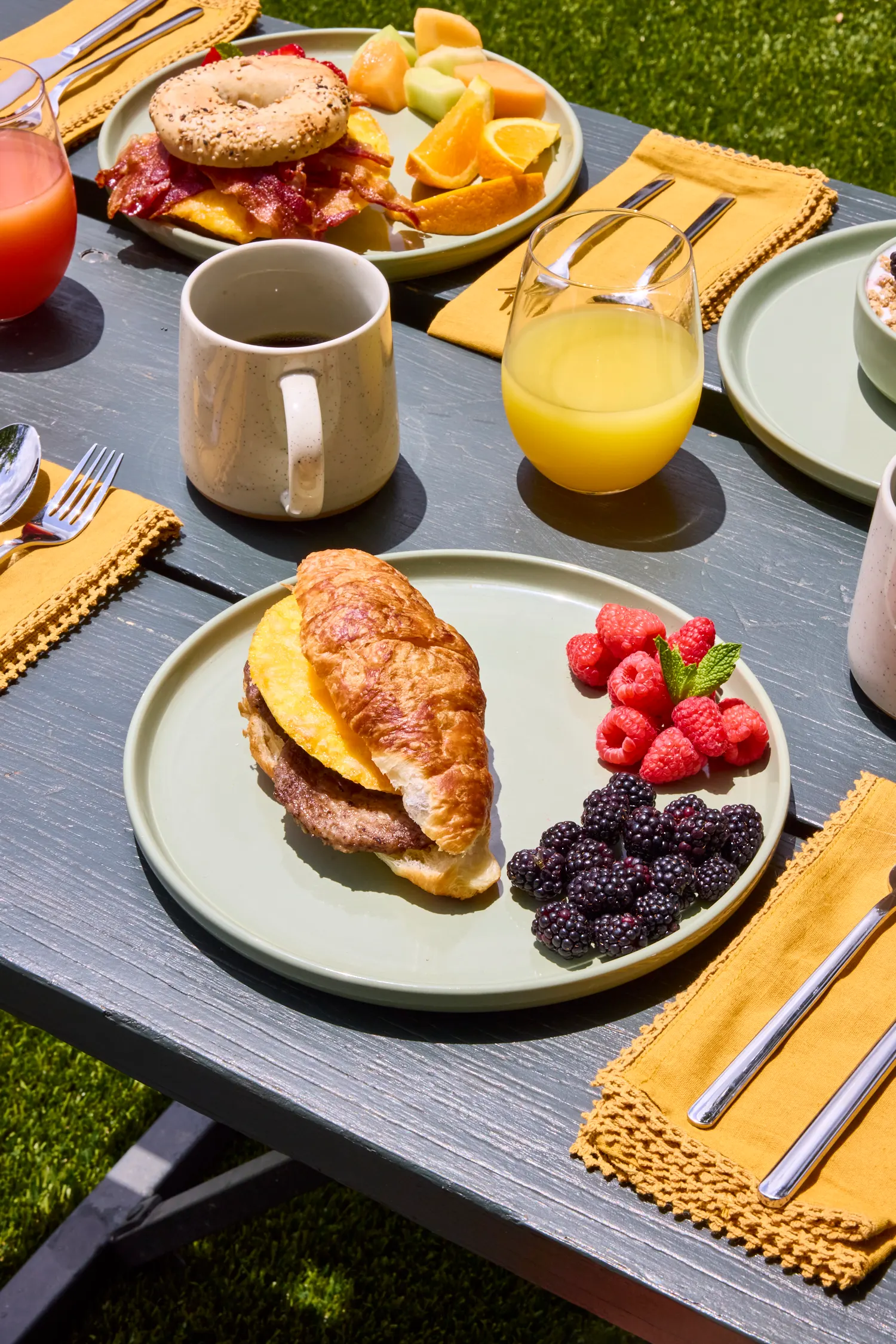 Breakfast croissant, bagel, berries and juice on a picnic table in the sun, La Piscine
