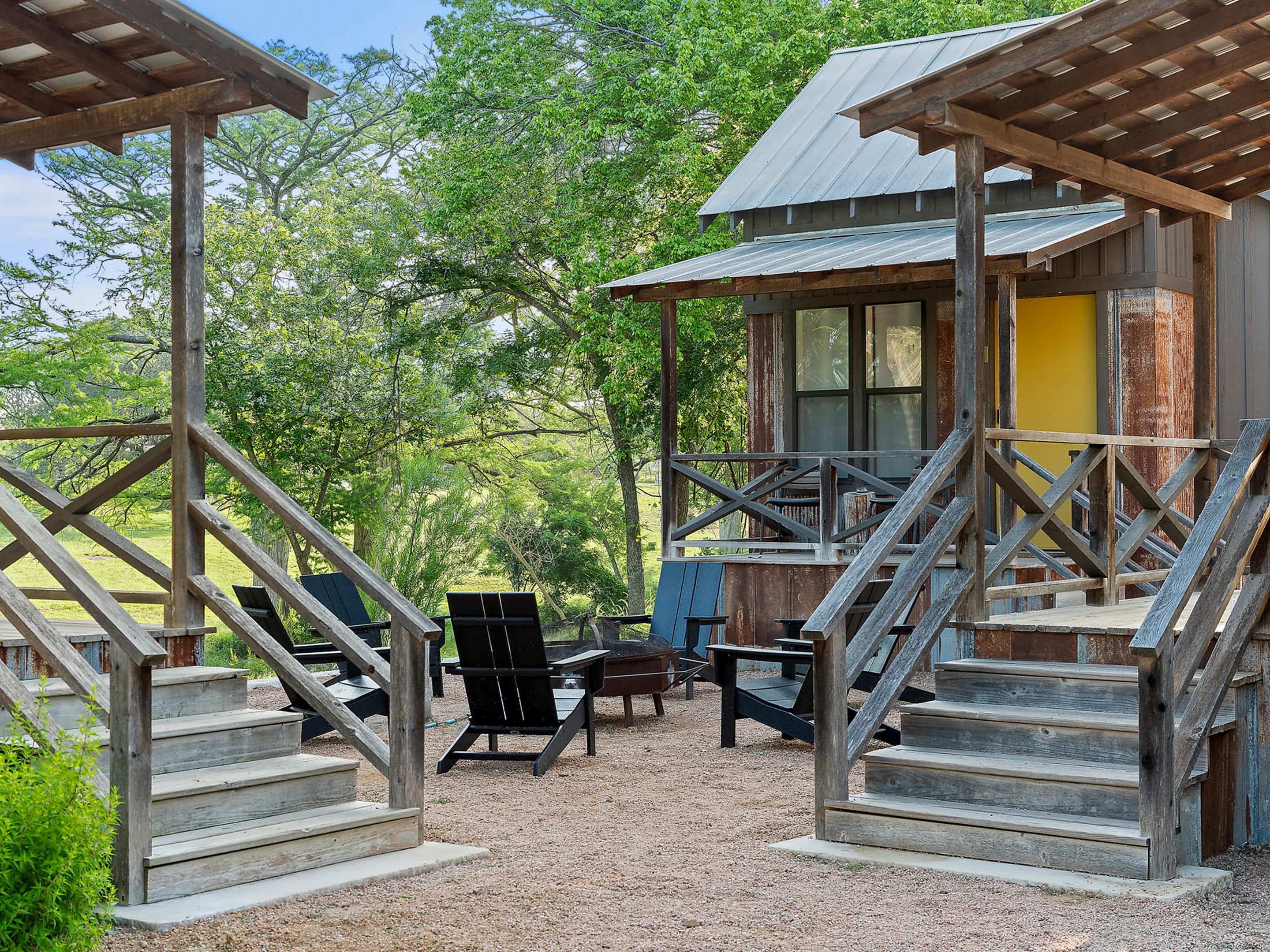 Two cabin porches facing a gravel court with a fire pit between them, Camp Comfort