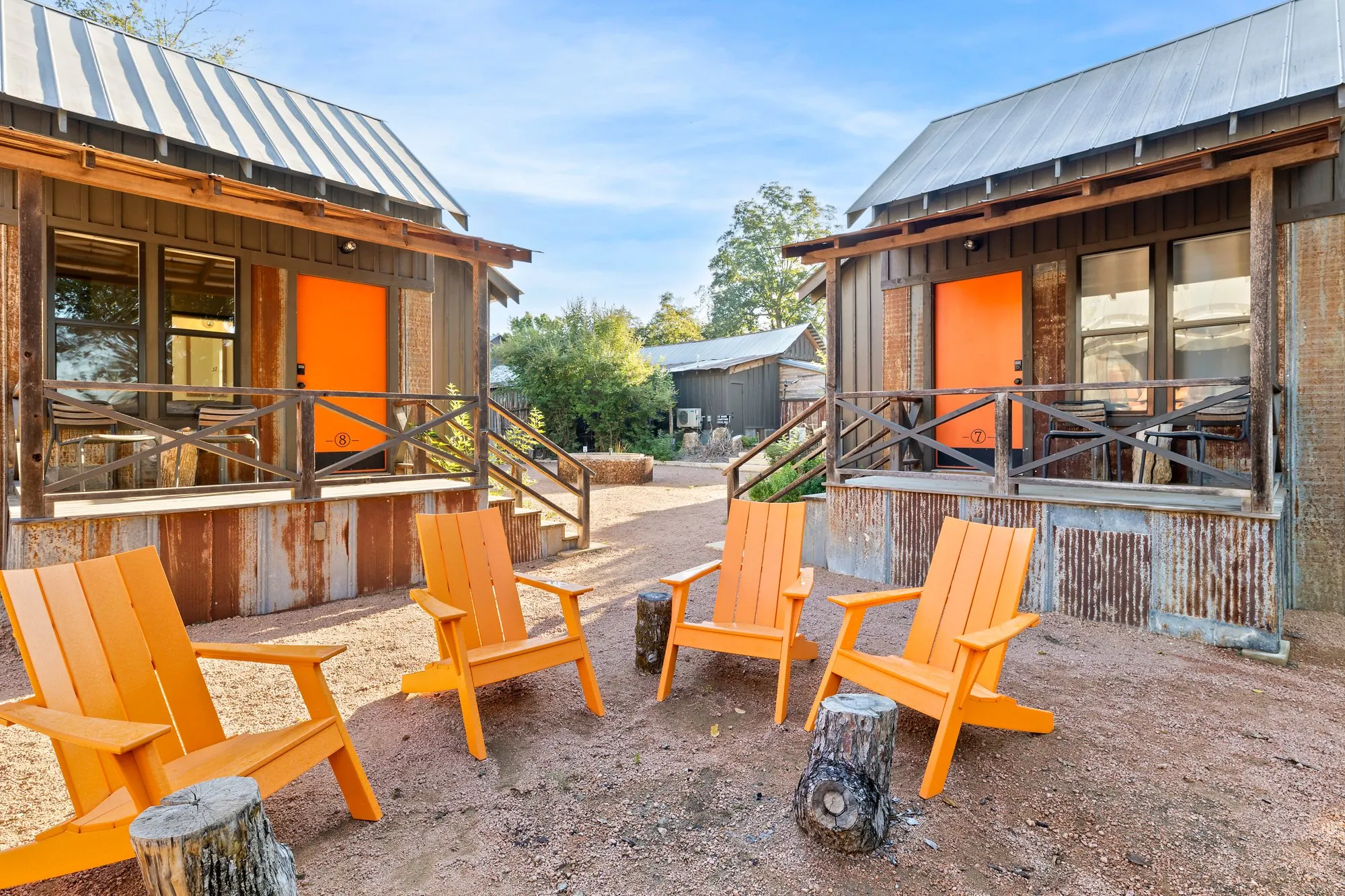 Two cabins with orange doors and Adirondack chairs on the gravel yard, Camp Comfort
