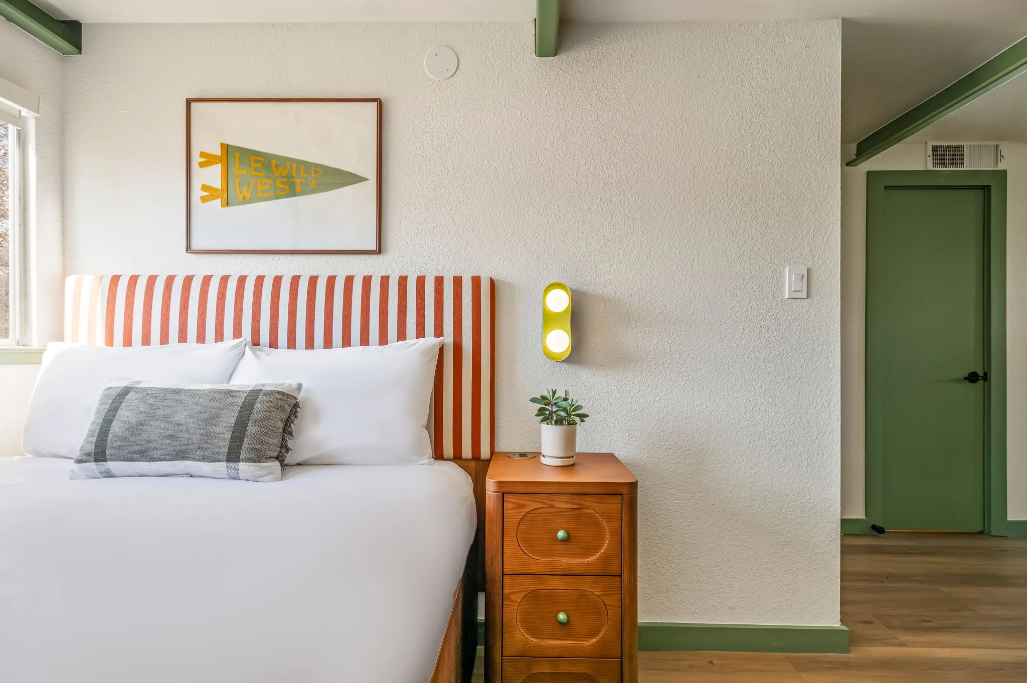 Room with a red-striped headboard, a framed Le Wild West pennant, oak nightstand and green trim