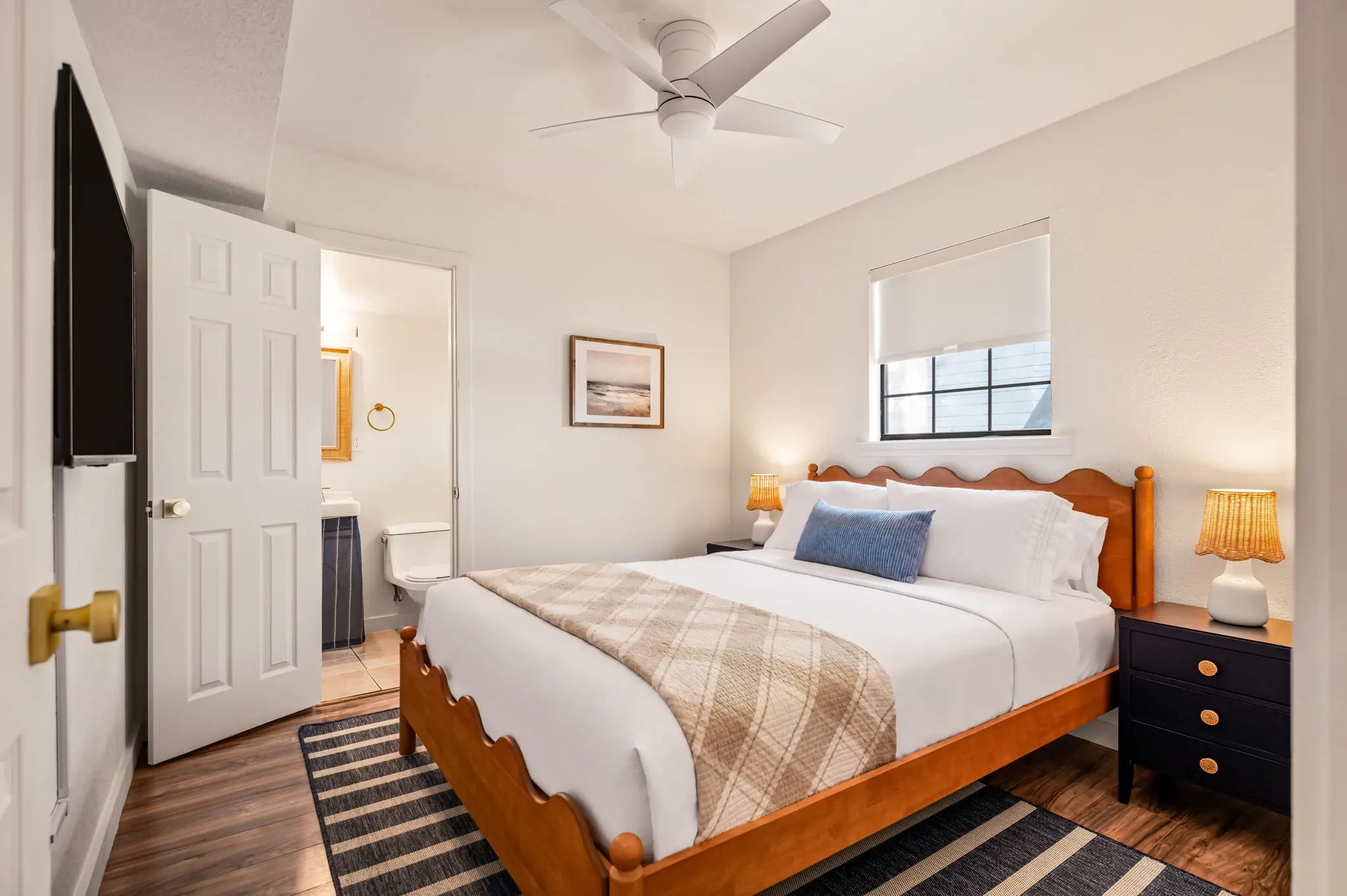 Loft bedroom with a scalloped wood bed, rattan lamps and striped rug, The Claire Hotel