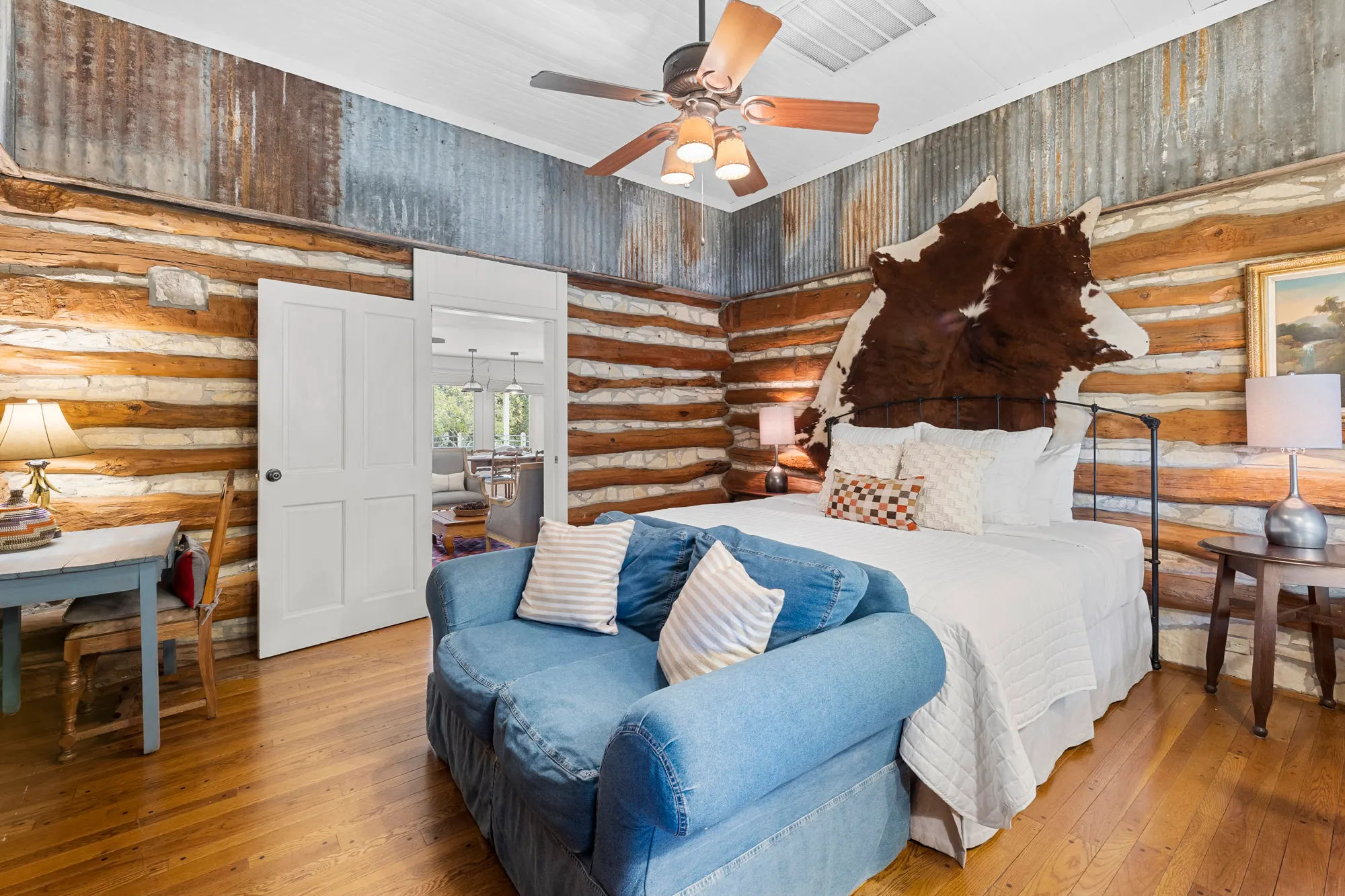 Log-and-limestone room with a cowhide over an iron bed and a denim loveseat, The Meyer Hotel