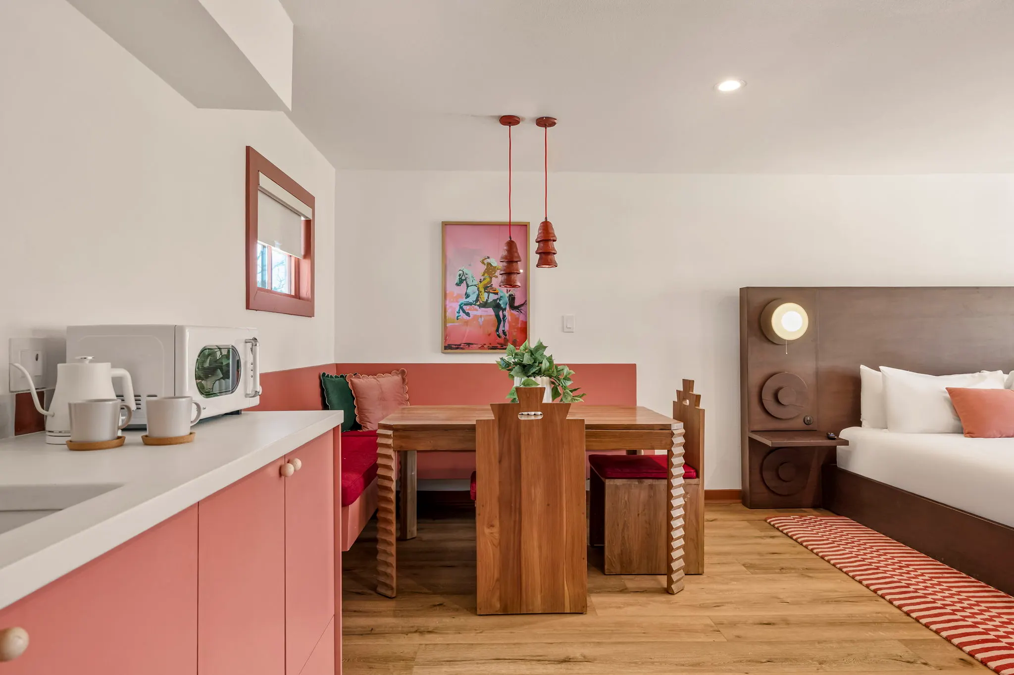 Studio with a pink kitchenette, carved teak dining nook, clay pendants and a cowboy print