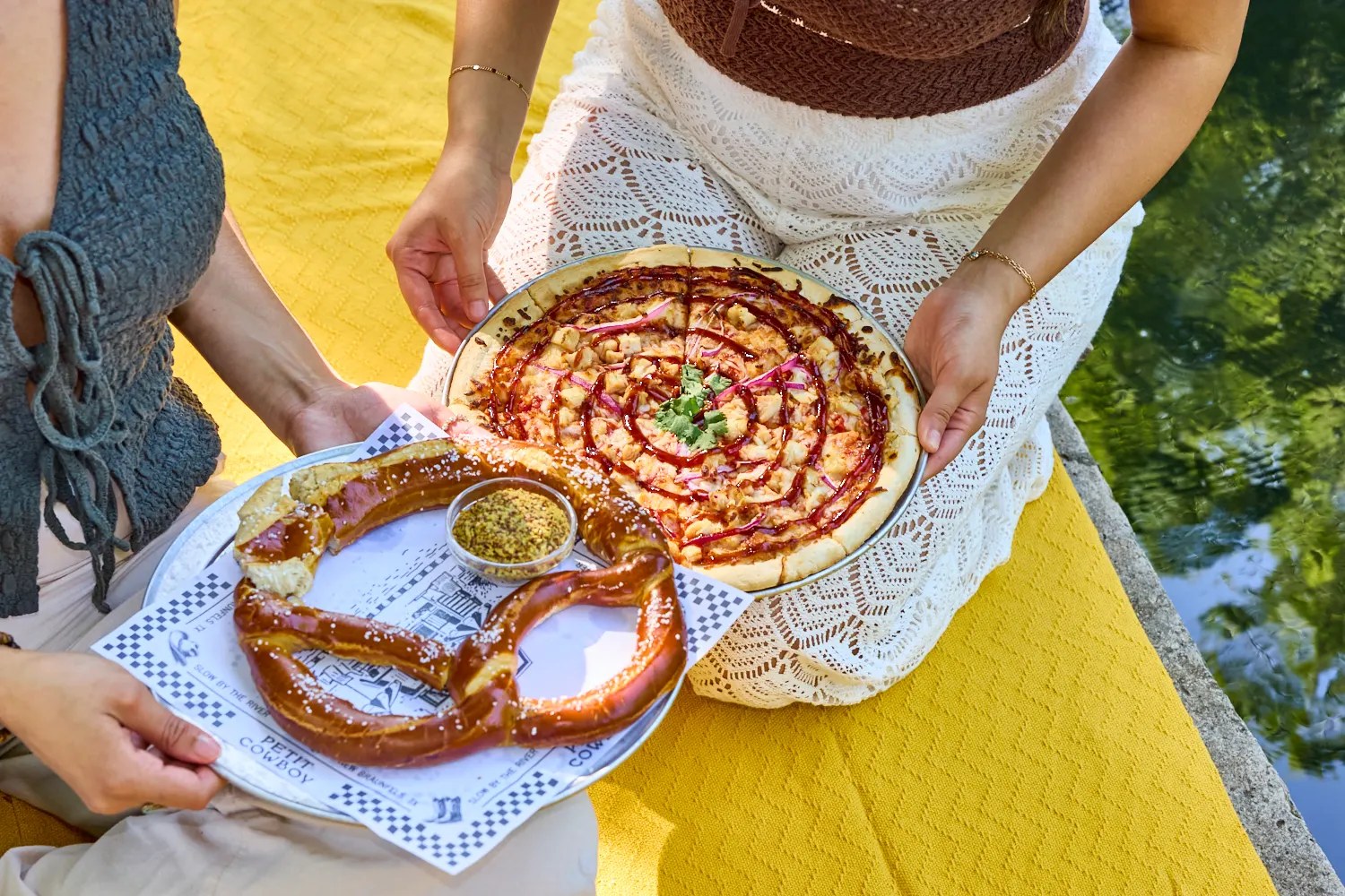 A giant pretzel with mustard and a barbecue chicken pizza held over the water, La Piscine
