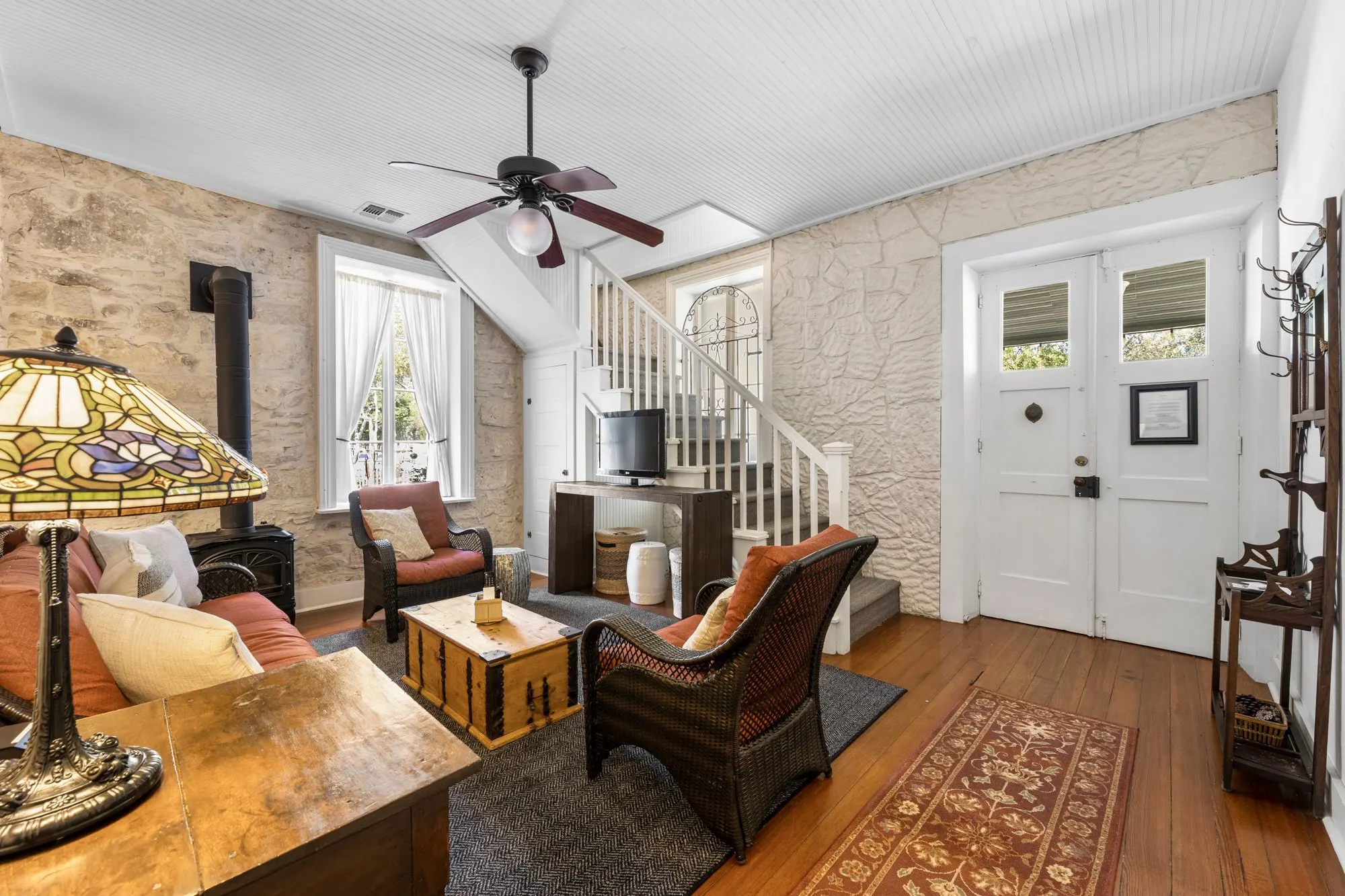 Limestone parlor with a wood stove, wicker chairs, a white stair and double front doors, The Meyer Hotel