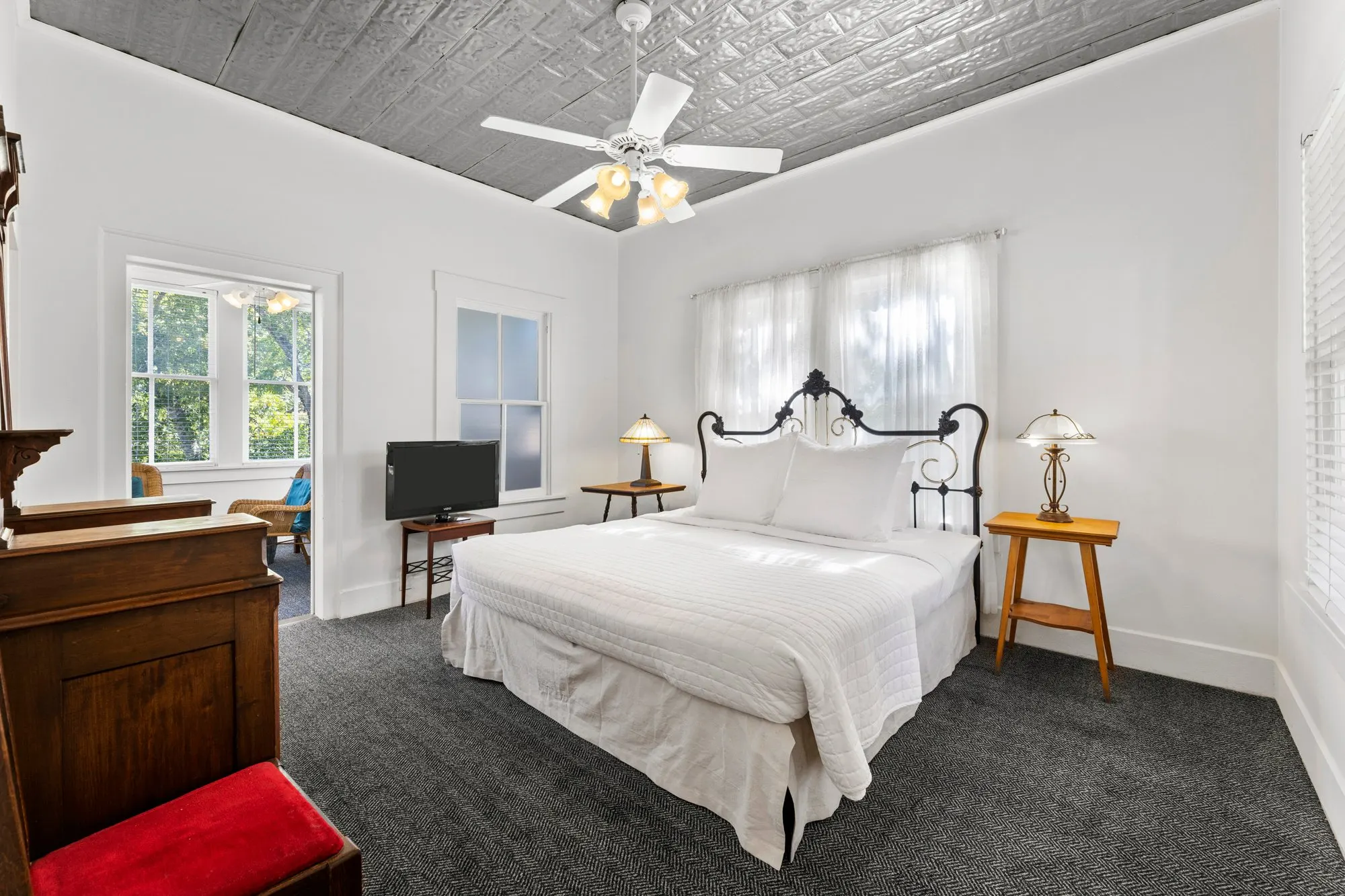 White room with an ornate iron bed under a pressed-tin ceiling, a sunporch through the door, The Meyer Hotel