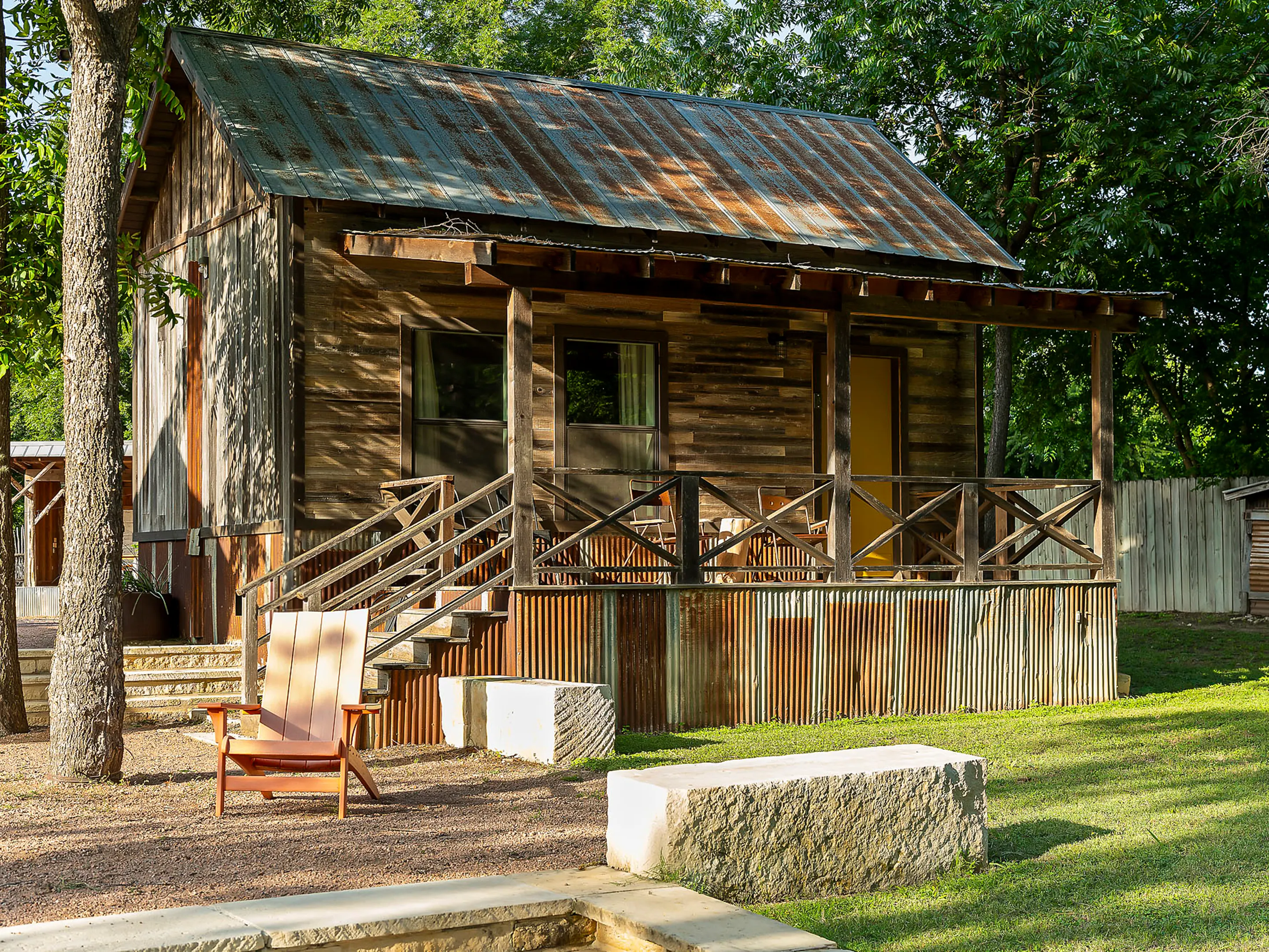 Reclaimed-wood cabin with a tin roof, yellow door and limestone benches, Camp Comfort