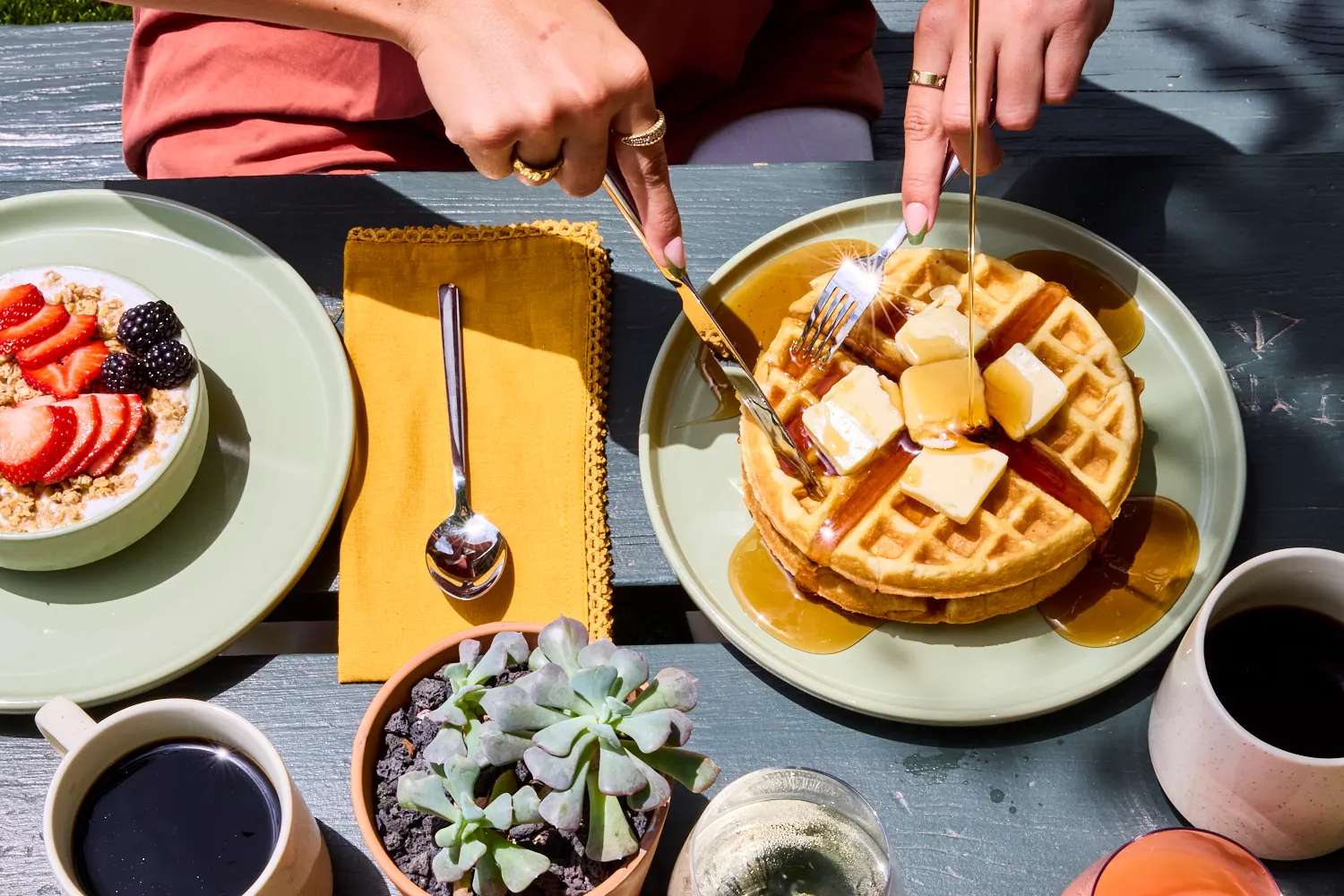 Waffles with butter and syrup being cut, granola bowl and coffee alongside, La Piscine